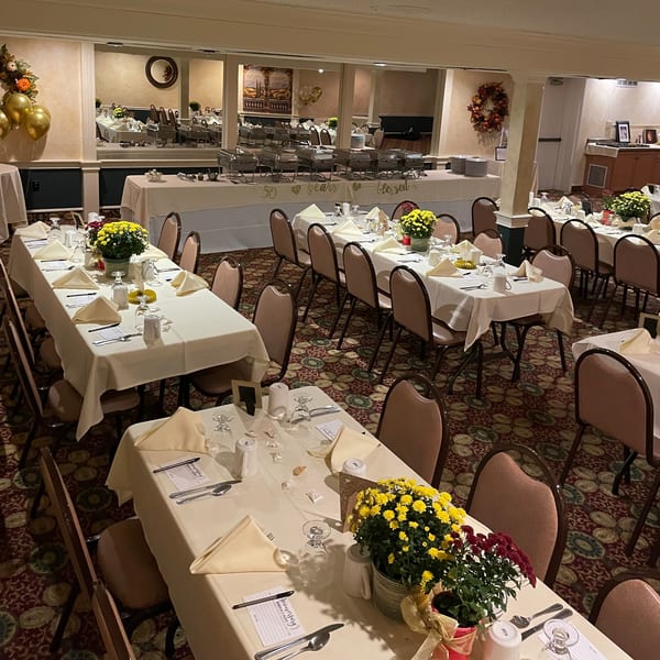 A large dining room set for an event, with multiple tables, chairs, and a buffet line.