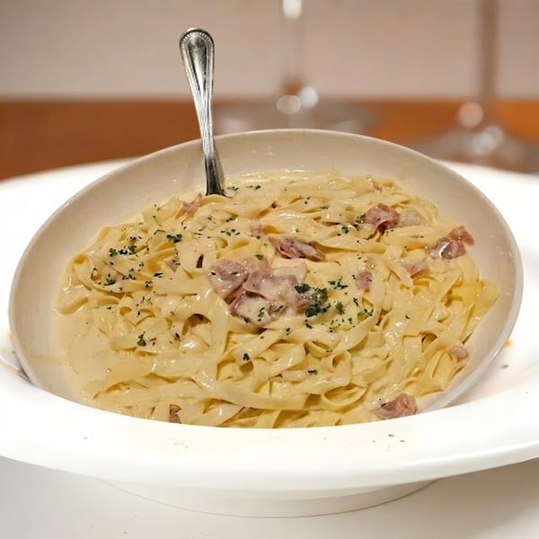 Creamy fettuccine pasta with bacon bits and parsley in a white bowl with a spoon.