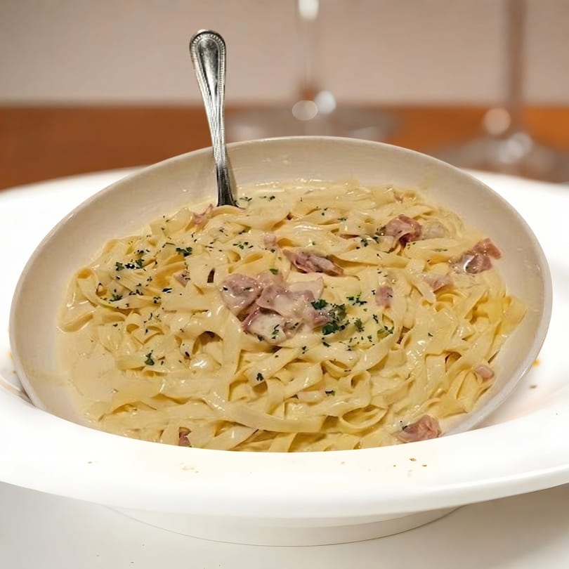 Creamy fettuccine pasta with bacon bits and parsley in a white bowl with a spoon.