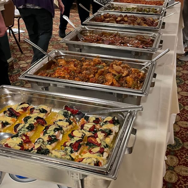 A buffet line with several chafing dishes filled with various hot foods, including fish, chicken, and potatoes.