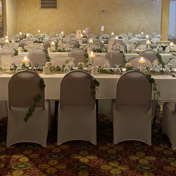 Elegant dining room with tables set with white tablecloths, candles, and greenery, ready for guests.