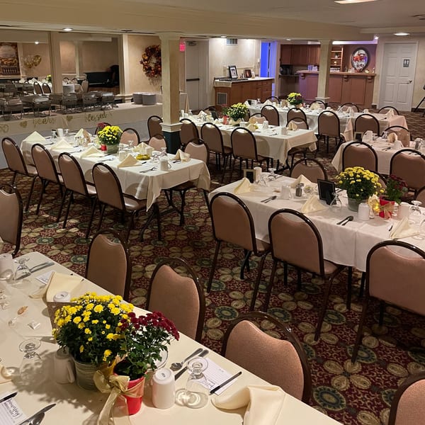 A banquet hall with multiple tables set with white tablecloths, place settings, and floral centerpieces.